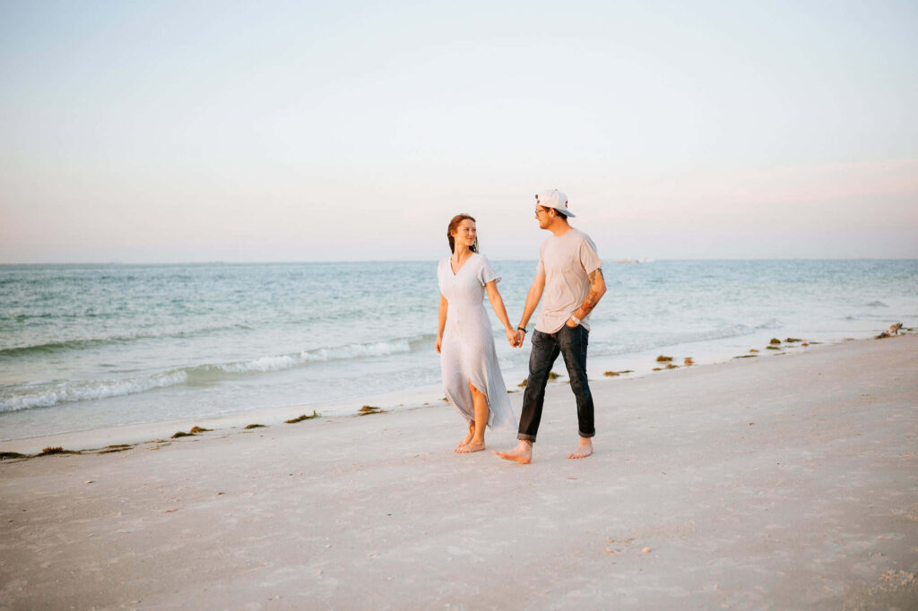 Couple is strolling down the beach hand in hand at Bean Point / Anna Maria Island at sunset. Captured by Atlanta Wedding photographers Peach State Weddings