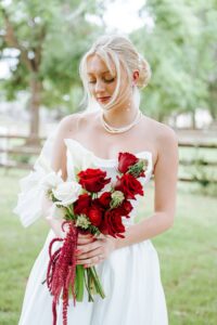 Lucy in her timeless white wedding gown holding her wedding bouquet with red and white roses. 