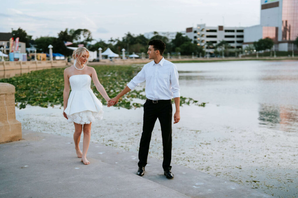 A couple walking along the Frances Langford Promenade at sunset, with the iconic Lake Mirror streetlights glowing in the background.