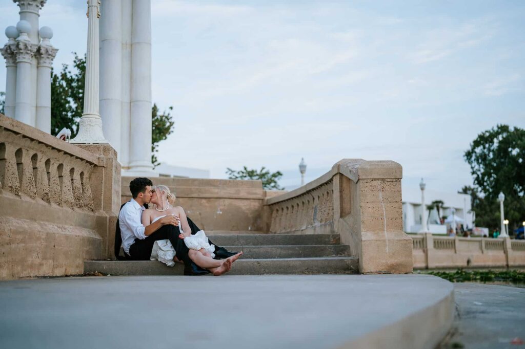 Bride and groom sitting on the stairs at Lake Mirror adjacent from the Magnolia Building, a Florida wedding venue in Lakeland.