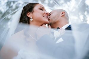 Wedding portrait of a veil shot with the groom kissing the bride's cheek on their wedding day at Bakers Ranch Wedding Venue