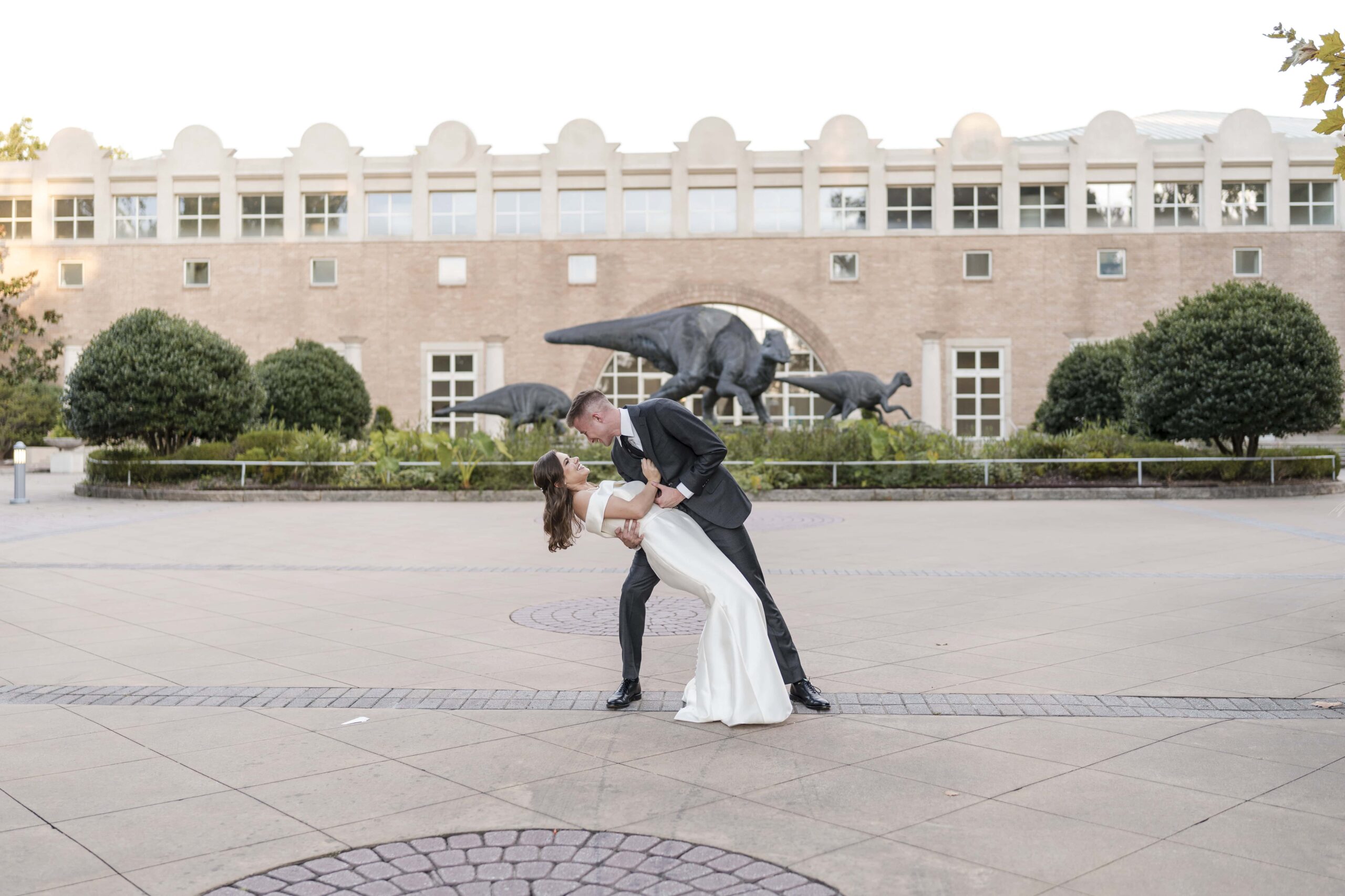 Groom is dipping his bride during sunset portraits in front of the Fernbank museum, a premier wedding venue in Georgia captured by Atlanta wedding photographer Peach State Weddings