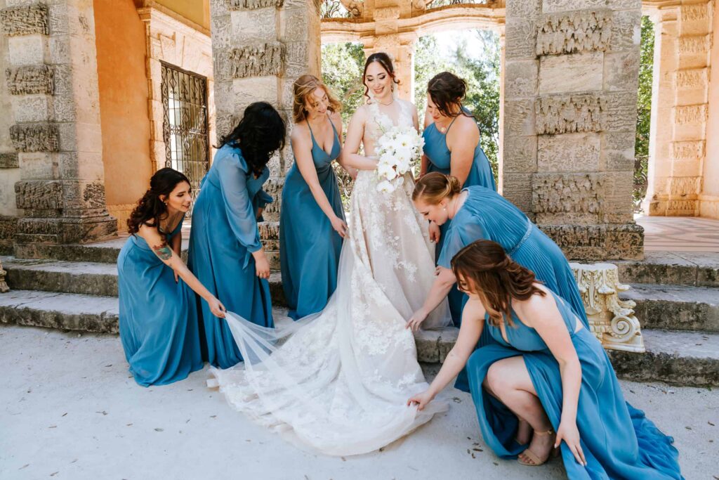 Atlanta Wedding photographer capturing Bridesmaids adjusting the bride's wedding gown during the bride's formals at Vizcaya Museum and Gardens Wedding in Miami Florida 