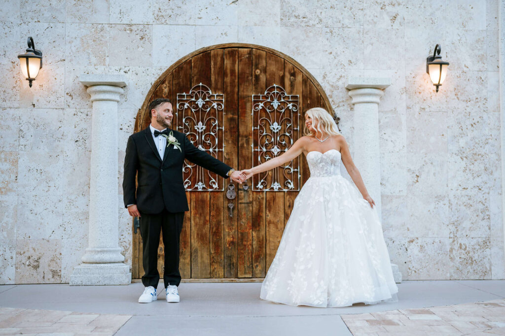 Portfolio 16 Bride and groom holding hands and looking at each other in front of the rustic wooden door just before their jewish wedding at Bakers Ranch Wedding Venue in Tampa, Florida.