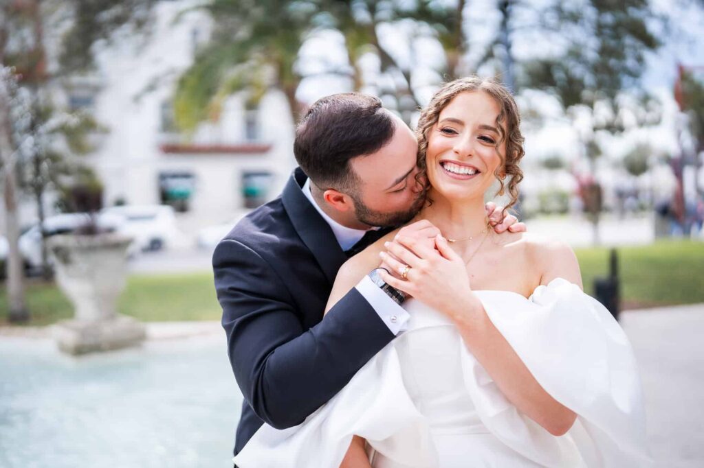 Groom kisses his bride on the neck in front of the the Casa Monica Fountain in St Augustine, FL - photographed by Atlanta GA Wedding Photographer
