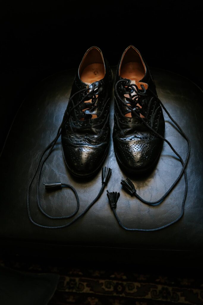 Close-up of traditional Scottish ghillie brogues with long laces on a dark leather chair; wedding detail photography at Rhodes Hall.