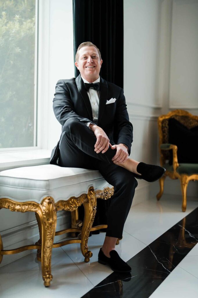A high-end wedding portrait of a groom in a tuxedo, framed by large windows at the World Equestrian Center.