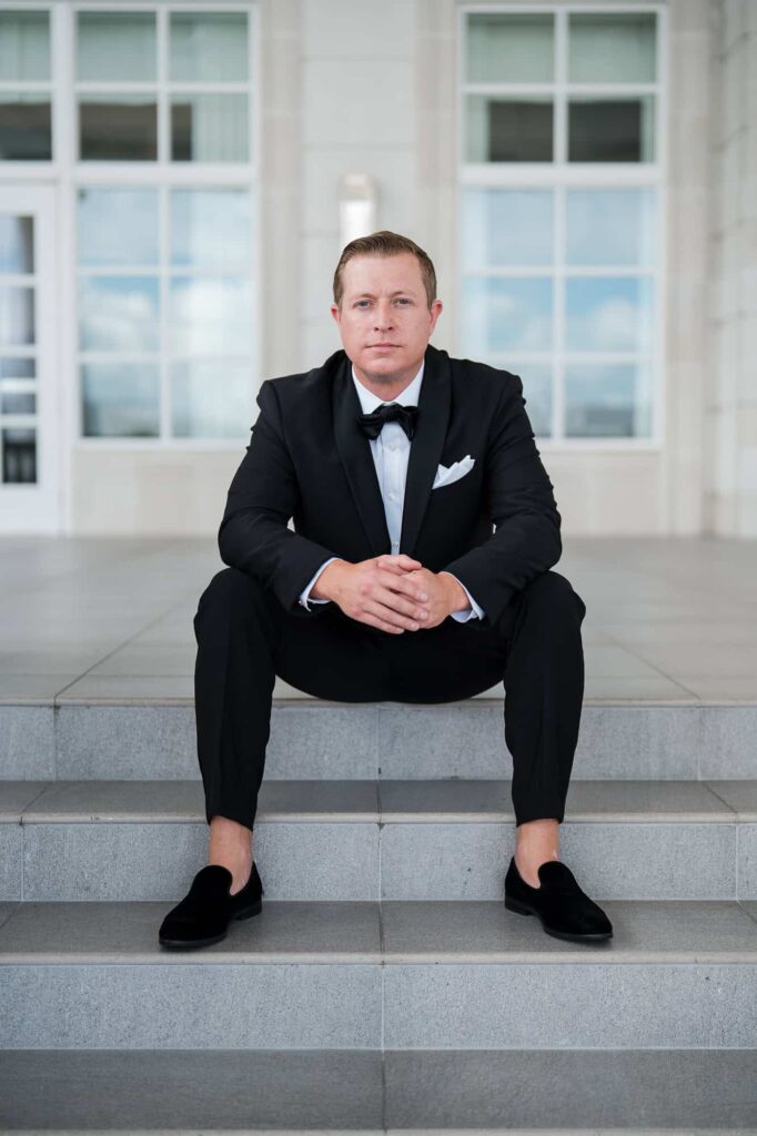 A modern, editorial portrait of a groom sitting on white steps at the World Equestrian Center, photographed by an Atlanta Georgia destination wedding photographer.