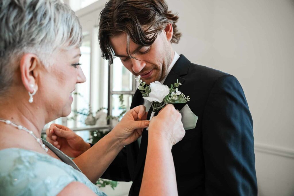 Fayetteville photographer capturing the groom's mother pinning the boutonniere on her son just moments before the wedding ceremony at the venue at daisy hill