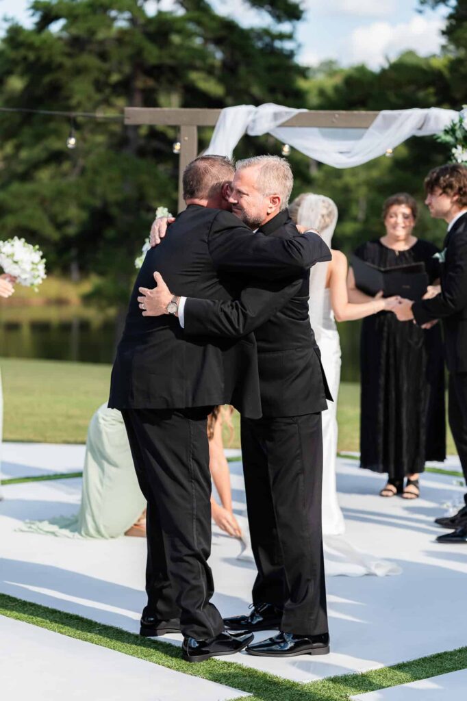 father and stepfather hugging at their daughter's wedding at the venue at daisy hill
