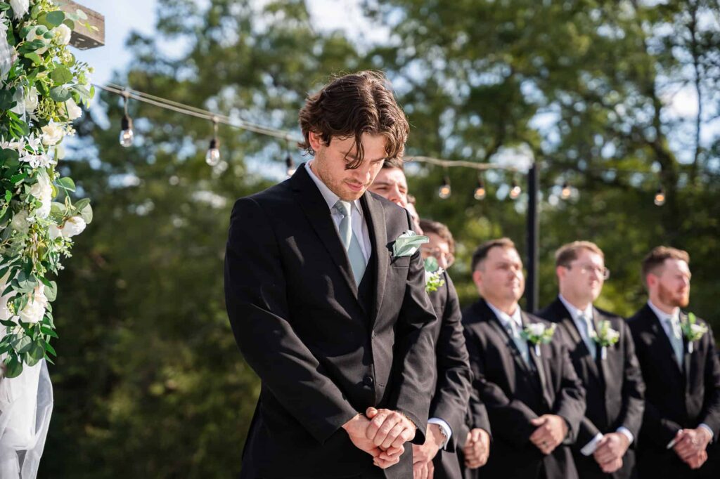 Zach standing at the altar as hannah walks down the aisle during the wedding ceremony at Daisy Hill, framed by the venue's signature greenery.