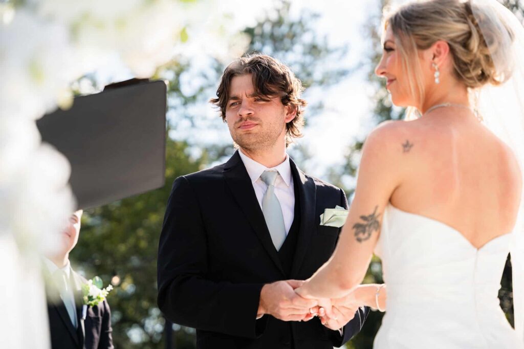 Close-up of the bride and groom holding hands during wedding vows at a modern barn ceremony in Fayetteville, GA.