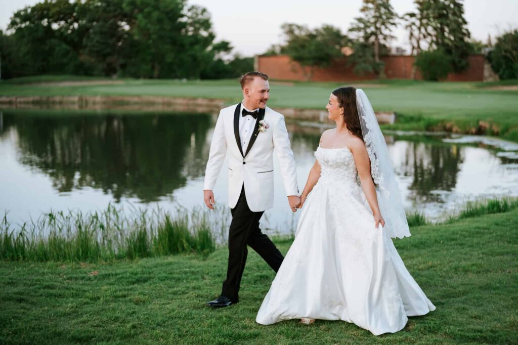 Atlanta wedding photographer capturing a candid moment of a bride and groom walking hand-in-hand by a lake at a country club wedding